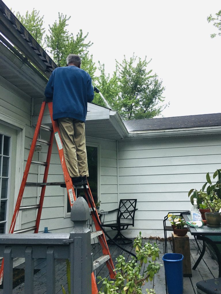 homeowner using a hose to spray out his home’s gutters